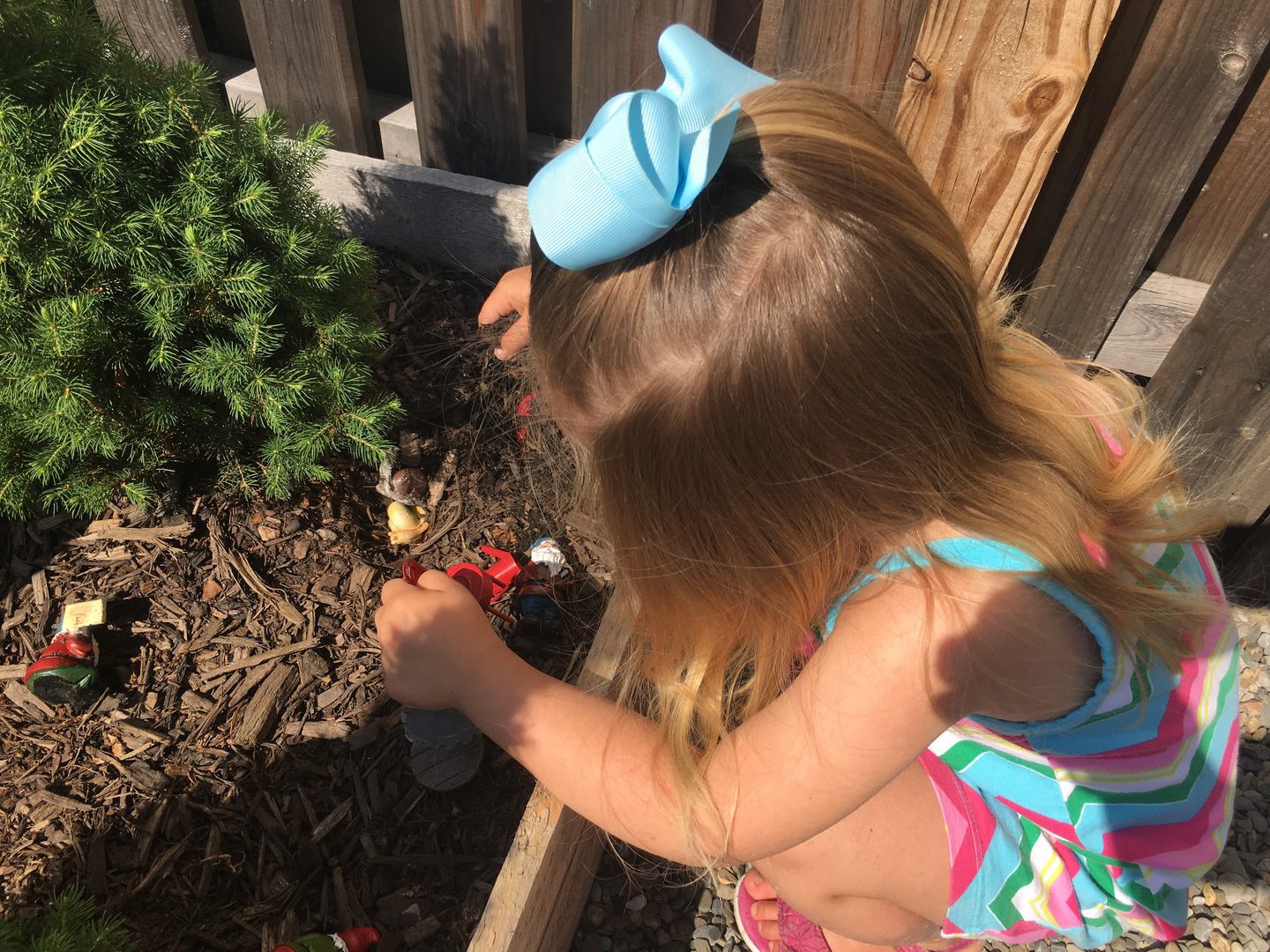 Child playing with toys in garden bed.