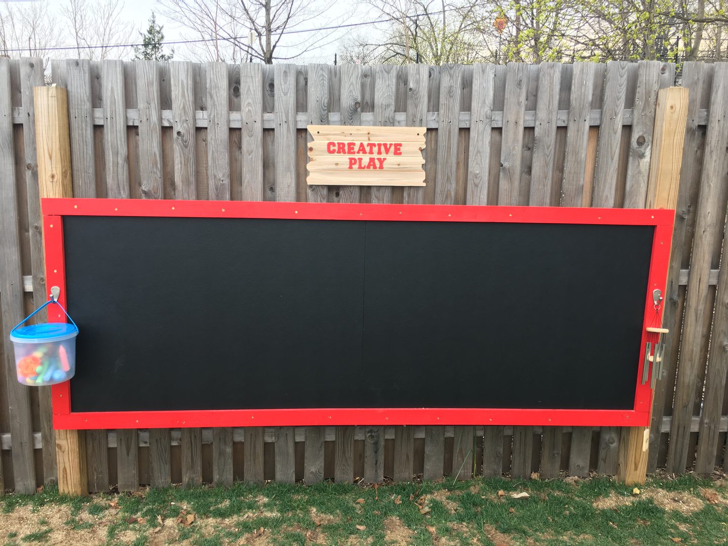 Outdoor chalkboard with red frame on fence.